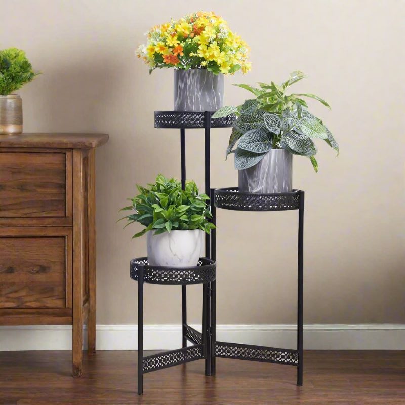 3-tier black metal plant stand displaying potted indoor flowers and green houseplants.