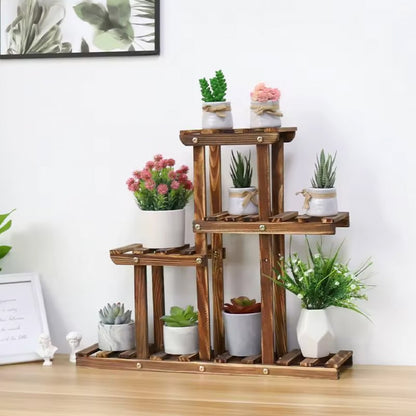 A rustic wooden three-tier plant stand with slatted shelves, styled with various potted succulents and artificial green plants on a light wood tabletop against a white wall.
