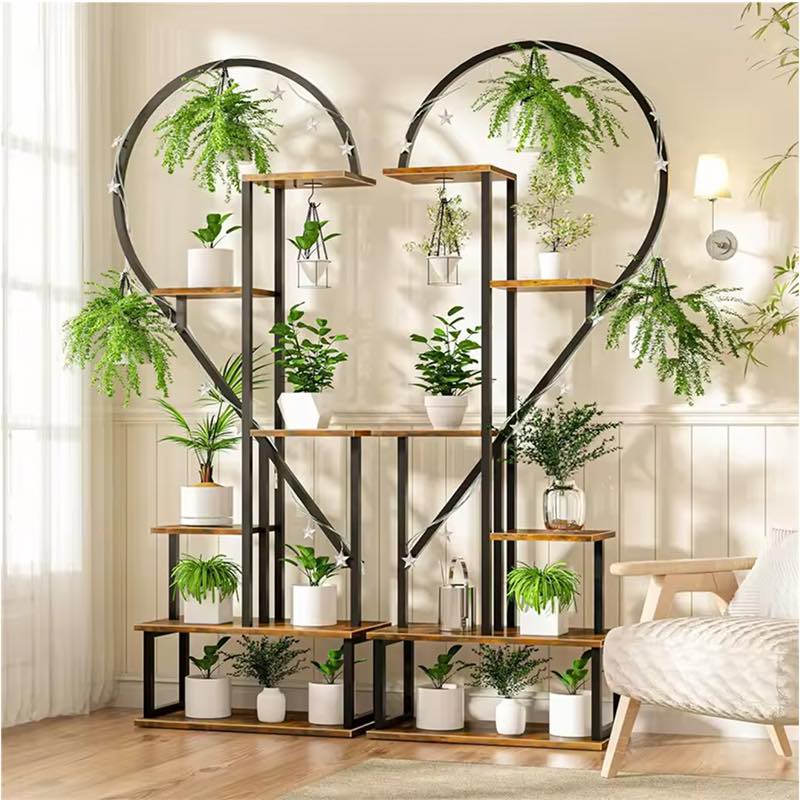 A large decorative metal plant stand shaped like two interlocking heart halves, with multiple wooden shelves and hanging green plants, shown in a bright living room next to a chair.